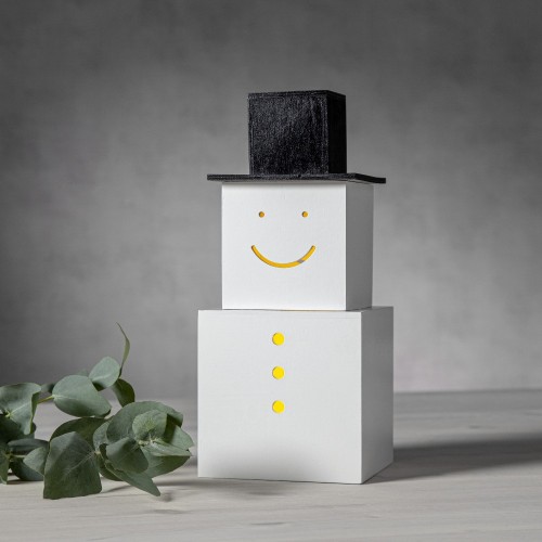 Dekoracja stołowa LED w formie bałwanka z białych kostek i czarnym kapeluszem; ciepłe światło widoczne w oczach, uśmiechu i guzikach, ustawiona na jasnym blacie w spokojnej, zimowej aranżacji.