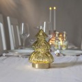 Szklana choinka LED z zielonego szkła stojąca na stole; w środku delikatne, ciepłe światło, w tle talerze, kieliszki i świece. Spokojna, świąteczna dekoracja do wnętrza.