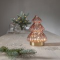 Choinka LED z przezroczystego, różowego szkła na jasnym stole; delikatne, ciepłe światło w środku, w tle gałązka i drobne dekoracje. Spokojna, elegancka dekoracja do wnętrza.
