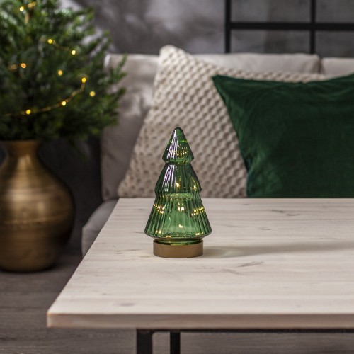 Szklana choinka LED z zielonego, przezroczystego szkła na jasnym stole; w środku ciepłe, miękkie światło, w tle sofa, poduszki i subtelne świąteczne dekoracje. Spokojna, przytulna ozdoba do wnętrza.