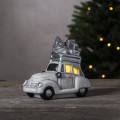 Dekoracyjny samochód w stylu retro, w białej i srebrnej kolorystyce, z choinką i prezentami na dachu, ustawiony na drewnianej powierzchni, świąteczna ozdoba w nastrojowym, przytulnym klimacie.