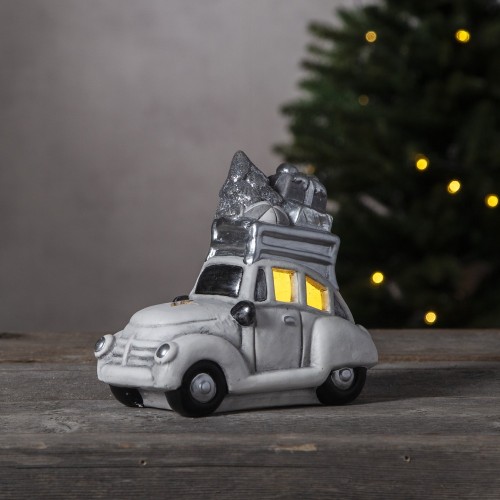 Dekoracyjny samochód w stylu retro, w białej i srebrnej kolorystyce, z choinką i prezentami na dachu, ustawiony na drewnianej powierzchni, świąteczna ozdoba w nastrojowym, przytulnym klimacie.