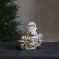 Figurka Mikołaja na motocyklu, złota dekoracja świąteczna LED na czarnym blacie, w tle rozmyta choinka, nastrojowy i przytulny charakter.