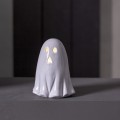 Ceramiczny duszek LED z delikatnie podświetlonymi oczami i ustami, ustawiony na gładkiej powierzchni na tle ciemnej ściany. Prosta forma i ciepłe światło budują subtelny, nastrojowy efekt.