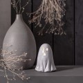 Ceramiczna figurka duszka z podświetlanymi oczami i ustami, ustawiona na półce obok matowego wazonu i suszonych gałązek. Ciepłe światło na ciemnym tle tworzy nastrojową, jesienną aranżację.