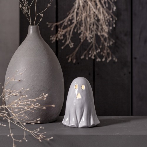 Ceramiczna figurka duszka z podświetlanymi oczami i ustami, ustawiona na półce obok matowego wazonu i suszonych gałązek. Ciepłe światło na ciemnym tle tworzy nastrojową, jesienną aranżację.