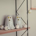 Dwie ceramiczne figurki duszków z podświetleniem LED ustawione na półce, obok girlandy z małymi lampkami w kształcie dyni. Ciepłe światło tworzy przytulną, halloweenową dekorację.