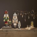 Kilka drewnianych figurek dziadka do orzechów w różnych rozmiarach, ustawionych na stole wśród dekoracyjnych światełek. Subtelne podświetlenie tworzy spokojny, nastrojowy klimat wnętrza.