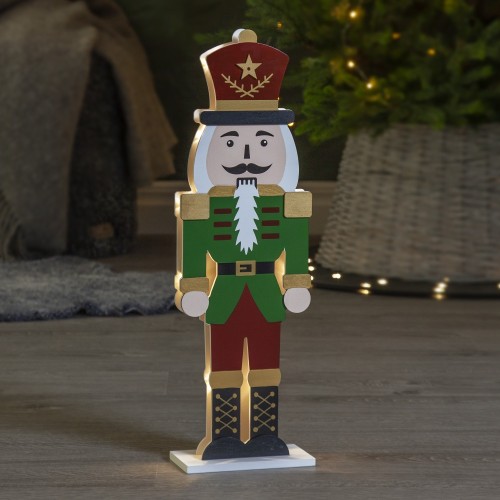 Drewniana figurka dziadka do orzechów w zielono-czerwonym stroju z podświetleniem LED, stojąca na podłodze w przytulnym wnętrzu. Ciepłe światło buduje spokojny, świąteczny nastrój.