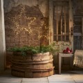 Dwie gwiazdy LED na metalowych stelażach z ciepłym światłem, ustawione w drewnianej beczce z zielonymi gałązkami. Przytulna, świąteczna aranżacja w rustykalnym wnętrzu.