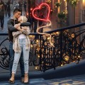 Romantyczna scena z parą obejmującą się na miejskim moście, obok świecące czerwone serce LED z liniowego światła. Ciepła iluminacja tworzy nastrojowy klimat walentynkowy w wieczorowej scenerii miasta.