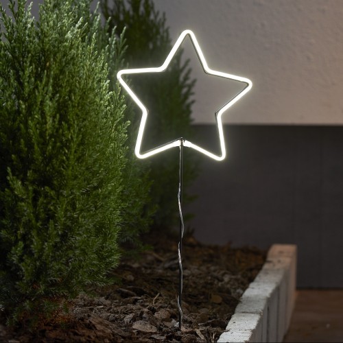 Gwiazda neon LED świecąca jasnym światłem LED na metalowym stelażu, dekoracja świetlna do ogrodu i wnętrz, umieszczona między roślinami przy ścianie budynku.