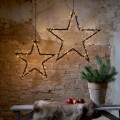 Dwie wiszące gwiazdy LED o różnych rozmiarach z ciepłymi punktami świetlnymi, zawieszone na łańcuchach na tle ceglanej ściany, dekoracyjna aranżacja z donicą i naturalnymi dodatkami.
