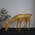 Złota dekoracja świetlna w kształcie jelenia z opuszczoną głową; drobne punkty światła LED odbijają się od błyszczącej powierzchni, aranżacja na ciemnym podłożu przy jasnej ścianie.