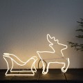 Dekoracja świetlna neon LED przedstawiająca renifera zaprzęgniętego do sań, ustawiona przy ścianie. Ciepłe światło tworzy wyraźny kontur sylwetek i nadaje całości przytulny, świąteczny charakter.
