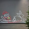 Dekoracja świetlna neon LED przedstawiająca Świętego Mikołaja na saniach z reniferem, ustawiona na półce przy ścianie. Białe, czerwone i zielone światło tworzy wyraźny kontur sceny o świątecznym charakterze.