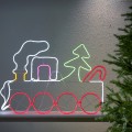 Dekoracja neon LED z motywem świątecznego pociągu, zamontowana przy ścianie obok choinki. Czerwone, zielone i białe światło podkreśla kształt lokomotywy i nadaje całości ciepły, świąteczny charakter.