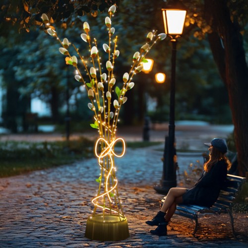 Dekoracja świetlna „Bazie w Bukiecie 3D” – wolnostojący bukiet z gałązek bazi z ciepłym światłem LED, ustawiony na alejce parkowej obok ławki i latarni, tworzący nastrojowy, przytulny klimat wieczorem.