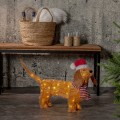 Dekoracja LED w kształcie psa z czapką i szalikiem, ustawiona we wnętrzu obok drewnianej ławki. Delikatne światło podkreśla detale sylwetki i nadaje przytulny charakter aranżacji.