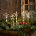 Świąteczna aranżacja z pięcioma dekoracjami LED w kształcie gwiazd na palikach umieszczonymi wśród zielonych gałązek ciepłe światło tworzy przytulny i harmonijny klimat dekoracyjny.