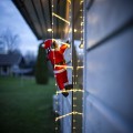 Świąteczna dekoracja LED z Mikołajem wspinającym się po drabinie świetlnej zamocowanej przy elewacji budynku emitująca ciepłe białe światło widoczna z bliska w plenerowym otoczeniu.