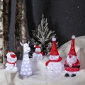 Świąteczna aranżacja z figurkami LED świecącymi białym światłem, przedstawiającymi bałwanki, Mikołaja i renifery, ustawionymi w śnieżnej scenerii z choinką oraz pniami drzew w tle.