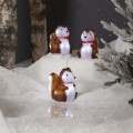 Zimowa aranżacja z figurkami LED w kształcie wiewiórek, świecącymi białym światłem, ustawionymi w śnieżnej scenerii z drzewami i dekoracyjną roślinnością.