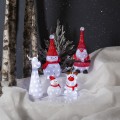 Świecące figurki LED przedstawiające Mikołaja, reniferki oraz bałwanki, ustawione na śnieżnej aranżacji z iglastymi gałęziami i pniami drzew.