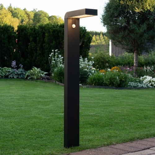 Czarna solarna lampa ogrodowa LED VICI w formie słupka z czujnikiem ruchu PIR zamontowana na trawniku nowoczesne oświetlenie zewnętrzne do ogrodu.