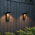 Dwa czarne solarne kinkiety LED VICI zamontowane na drewnianej ścianie ogrodu subtelne światło podkreślające strukturę drewna.