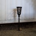 Solarny słupek ogrodowy LED z dekoracyjnym ażurowym wzorem, lampa solarna zewnętrzna świecąca ciepłym światłem przy ścianie budynku.