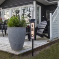 Lampa solarna LED do oznaczenia numeru posesji, podświetlany słupek adresowy z panelem słonecznym, umieszczony przy tarasie obok donicy z roślinami.