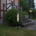 Solarny słupek LED do oznaczenia numeru domu, podświetlana tabliczka adresowa z panelem solarnym, ustawiona w ogrodzie przy schodach i wejściu do budynku.