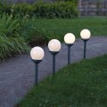 Cztery solarne lampy ogrodowe z mlecznym kulistym kloszem ustawione wzdłuż ścieżki na trawniku, emitujące równomierne białe światło LED.