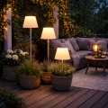 Trzy solarne lampy ogrodowe LED z białymi kloszami w kształcie abażuru ustawione w donicach na drewnianym tarasie obok sofy i stolika, dekoracyjne oświetlenie zewnętrzne do ogrodu i na taras.