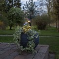 Solarny reflektor ogrodowy LED ustawiony w donicy na tarasie, z regulowaną głowicą i panelem solarnym na elastycznych ramionach, emitujący ciepłe białe światło akcentujące roślinność ogrodu.