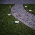 Solarne oprawy ogrodowe LED wpuszczane w trawnik z okrągłą obudową, rozmieszczone wzdłuż ścieżki jako punktowe oświetlenie ogrodu.
