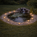 Solarne oprawy ogrodowe LED rozmieszczone wokół oczka wodnego, tworzą nastrojową iluminację podkreślającą linię kamiennej opaski i delikatnie akcentującą przestrzeń ogrodu po zmroku.