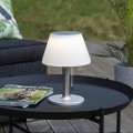 Solarna ogrodowa lampka stołowa LED z białym kloszem i metalową podstawą, ustawiona na stoliku tarasowym – dekoracyjne oświetlenie na balkon, taras i do ogrodu.