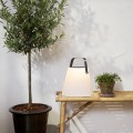 Solarna ogrodowa lampa LED z białym kloszem i uchwytem do przenoszenia, ustawiona na drewnianej półce wśród roślin, tworząca nastrojowe oświetlenie ogrodu, tarasu lub balkonu.