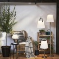 Solarne ogrodowe lampy LED z białymi kloszami w wersji stojącej, wiszącej i stołowej, ustawione przy ścianie tarasu wśród roślin i drewnianych dodatków.