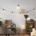 Solarna ogrodowa lampa LED z białym kloszem zawieszona nad tarasem, uzupełniona stojącymi modelami i dekoracyjną girlandą świetlną w przytulnej aranżacji.