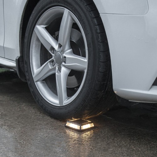 Samochód na podjeździe z kołem nad solarną lampą najazdową LED w czarnej obudowie, niskoprofilowe oświetlenie podjazdu, wjazdu do garażu i miejsc parkingowych.