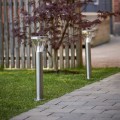 Dwie solarne lampy ogrodowe LED w srebrnej obudowie przy ścieżce z kostki brukowej, dekoracyjne oświetlenie trawnika i przestrzeni wokół domu.