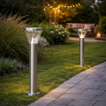 Dwie solarne lampy ogrodowe LED w srebrnej obudowie ustawione przy kostce brukowej i trawniku, dekoracyjne oświetlenie ogrodu i przestrzeni wokół domu po zmroku.