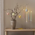 Porcelanowe dekoracje wielkanocne LED w kształcie kurczaczków i jajek zawieszone na gałązkach w wazonie obok pastelowych świec stołowych, ozdoby do wnętrz emitujące ciepłe światło.