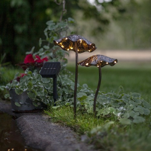 Solarne lampy ogrodowe LED w kształcie grzybów z metalowymi kapeluszami, ustawione przy rabacie z roślinami i widocznym panelem solarnym na szpikulcu. Dekoracyjne oświetlenie solarne do ogrodu, na trawnik lub wzdłuż ścieżki.