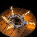 Girlanda LED z żarówkami G95 spiral filament w wersji białej, ciepłe światło na drewnianym stole, dekoracyjne oświetlenie wnętrza.