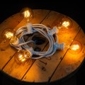 Girlanda świetlna z żarówkami LED E27 ułożona na drewnianej szpuli kabla. Ciepłe światło dekoracyjne idealne do ogrodu, tarasu lub wnętrz.