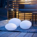 Trzy solarne lampy LED w kształcie kamieni świecące delikatnym światłem na dywanie tarasowym przy meblach ogrodowych. Dekoracyjne oświetlenie solarne do ogrodu i na taras.